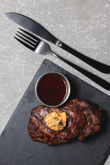 Grilled beef steak medium rare with sauce on black wooden cutting board with utensils. Copy space, flat lay.
