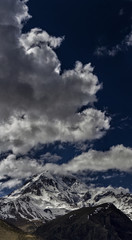 Obraz premium Clouds in the blue sky hit the top of the magnificent Kazbek. Mountain landscape panorama.