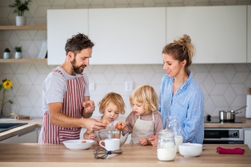 Young family with two small children indoors in kitchen, cooking.