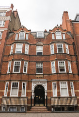 Fototapeta na wymiar Grenville mansions, Hunter Street, London, United Kingdom, England. June 2019. Beautiful vertical shot of this red brick building (black metal fence in front of it). Cloudy day in the english capital
