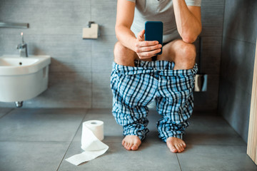 Young man using modern smartphone in toilet