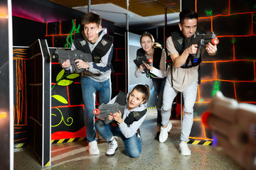 Ordinary Laser tag players young mens and womens playing in teams in dark laser tag station