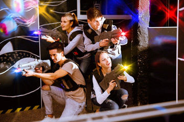 Happy young people with laser pistols posing together on dark la