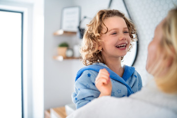 A cute small girl with unrecognizable mother in bathroom indoors at home.