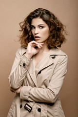 beauty fashion model with clean skin and curly hair in biege cloak stretch with scarf on biege background