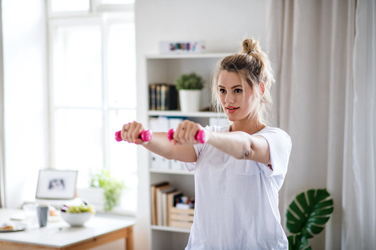 Young woman with dumbbells doing exercise in bedroom indoors at home. - Powered by Adobe