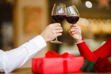 Hands holding glasses of wine on restaurant background. Couple clink glasses with red wine. Romance at restaurant for Valentine's Day- concept. Relationship & Birthday concept.