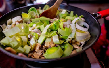 Selective focus on an unidentifiable chef's hand stirring a leek, chicken and bacon pasta dish cooking on the hob