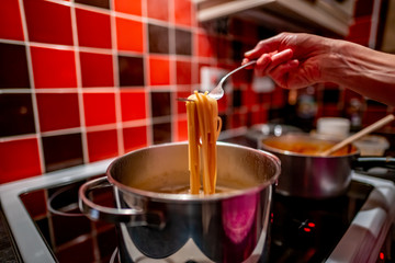  Selective focus of unidentifiable chef holding a fork of steaming spaghetti checking to see if it is cooked