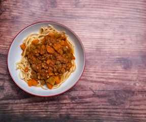 Flat lay of a bowl of lentil spaghetti bolognese on a wooden background with copy space