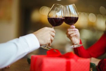 Hands holding glasses of wine on restaurant background. Couple clink glasses with red wine. Romance at restaurant for Valentine's Day- concept. Relationship & Birthday concept.