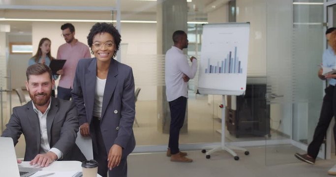 Cheerful group of multi ethnic workers applouding and standing in office room. Women and men office workers meeting and greeting somebody looking happy, gesturing good.