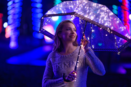 A girl walks through the night city with lights. Rainy. With an umbrella with lights.