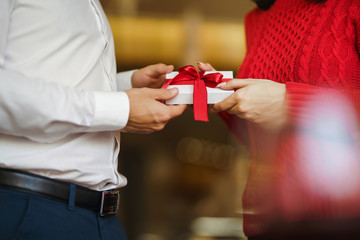 Man gives to his woman a gift box with red ribbon. Hands of man gives surprise gift box for girl. Lovers give each other gifts. Young loving couple celebrating Valentine's Day. Romantic day.