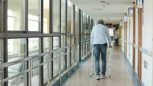 rear view of asian senior man walking using walker in hallway of nursing home or hospital