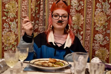 young woman eating Christmas dinner with a hat from a cracker on her head 