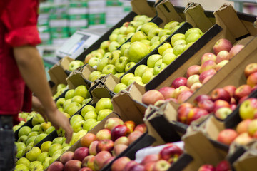 Young man seller lays out fresh fruits of the box on the grocery store