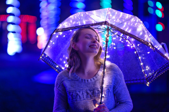 Girl at midnight in the rain with an umbrella and lights. Color and creative light. Art photo. Horizontal