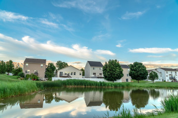 Naklejka na ściany i meble Scenic suburban landscape with homes and cloudy sky reflected on a shiny pond