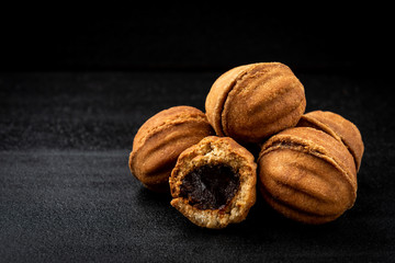 Shortbread in shape nut with caramel on black background.
