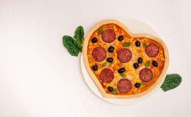 Tasty hot pizza in the shape of a heart with sausage, corn, cheese and olives on a white isolated background. Italian dish for Valentine's day. View from above. Valentine's day dinner