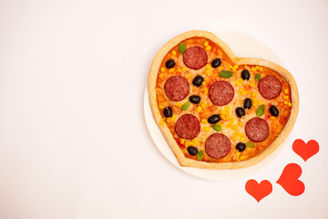 Tasty hot pizza in the shape of a heart with sausage, corn, cheese and olives on a white isolated background. Italian dish for Valentine's day. View from above. Valentine's day dinner
