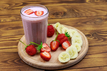 Glass of fresh smoothie of strawberry and banana on a wooden table