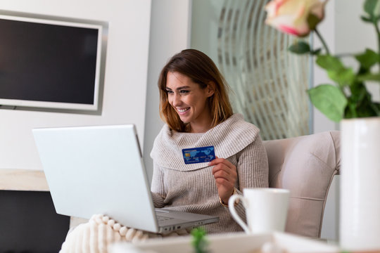 Young woman holding credit card and using laptop computer. Online shopping concept. Happy woman doing online shopping at home