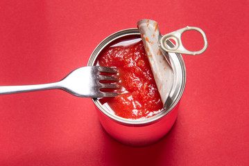Opened tin can with canned tomatoes, on red background
