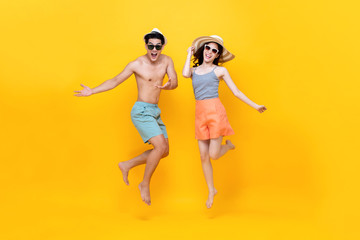 Playful energetic couple in summer beach casual clothes jumping on yellow background