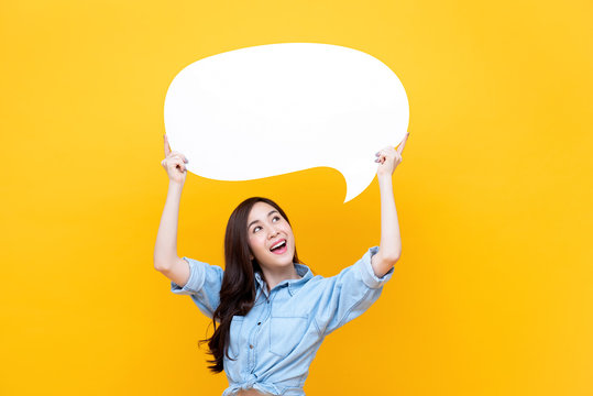Excited young beautiful Asian woman holding and looking up to speech bubble
