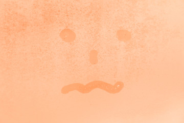 Fototapeta premium The picture or figure of the scared or tired face on the orange or pink evening or morning window glass with drops 