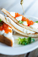 Classic breakfast, hot sandwich with red salmon caviar and mozzarella on a plate on a wooden table.