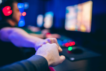 Professional gamer greeting and support team fists hands online game in neon color blur background. Soft focus, back view