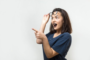 Happy young caucasian female in a blue shirt with glasses pointing fingers away, showing copy space for your text.