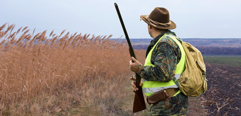 A hunter with a gun in his hands in hunting clothes in the autumn forest in search of a trophy. A...
