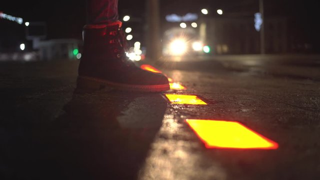 A girl stands at a pedestrian crossing and waits when you can cross the road. The traffic light is built into the asphalt, the green and red lanes are switched.
