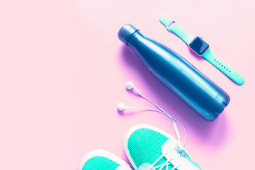 Exercise equipment flat lay in bold saturated colors: reusable zero waste bottle, sneakers, head phones and smart watch