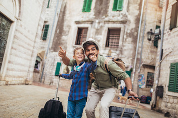 Fototapeta na wymiar Handsome man and his little son going to vacations, they pull their suitcases.