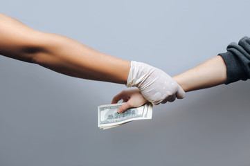 Hand of a woman patient gives money in the form of hundred-dollar bills to the doctor in a white...