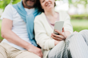 Married couple sit on the grass taking photos.