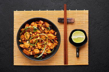 Kung Pao Chicken or Gong Bao Ji Ding at dark slate background. Sichuan Kung Pao is chinese cuisine dish with chicken meat, chilli peppers, peanuts, sauces and onion. Top view