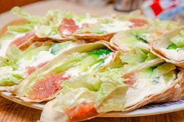 Fototapeta na wymiar Tortilla rolls with salmon, tender cheese, lettuce and fresh cucumber close-up on a plate