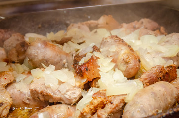 Sausages and pieces of meat fried with onions in a pan close up