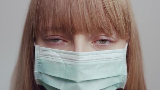 Young serious woman wearing a medical mask and looking in camera. Slowmotion