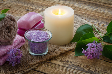 Towel, soap, candle and lilac flowers on wooden background.