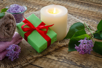 Towel, gift box, candle and lilac flowers on wooden background.