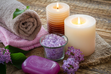 Towels, soap, candles and lilac flowers on wooden background.