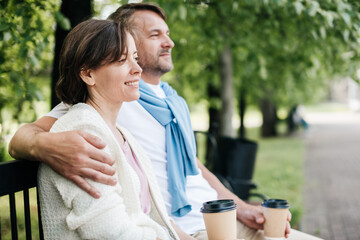 Married couple sit on the bench hugging in the park.