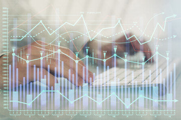 Double exposure of graph with man typing on computer in office on background. Concept of hard work.